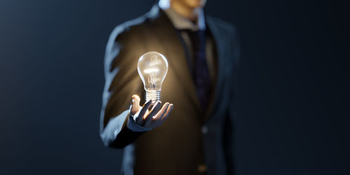 Midsection of man light bulb against black background