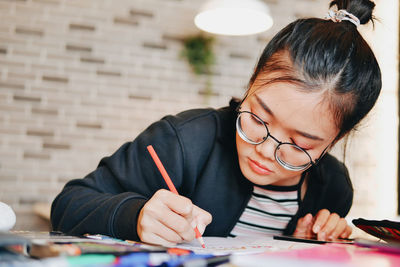 Young woman writing homework while sitting against wall at home