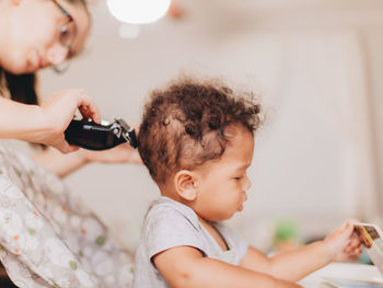 Midsection of mother trimming hair of son at home