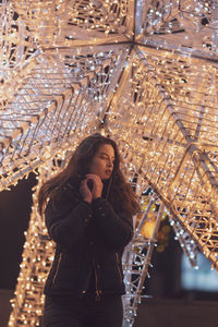 Woman wearing warm clothing against illuminated decoration at night