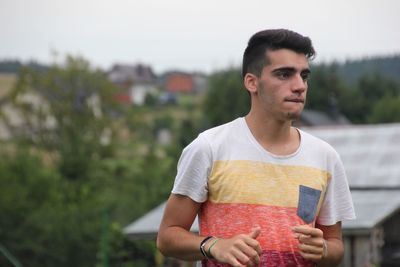 Portrait of young man holding camera against sky