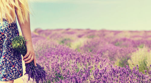 Rear view of woman standing on field of flowering plants against sky