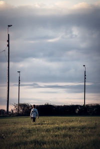 Rear view of boy walking on grassy field against sky