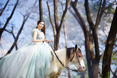 Low angle view of young woman riding horse in forest