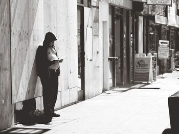 Side view of young man standing on footpath against building