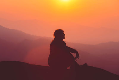 Silhouette man standing on rock against sky during sunset