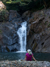 Rear view of woman man sitting by waterfall