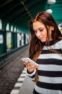 Young woman using mobile phone while standing at railroad station