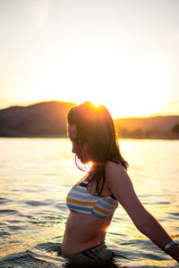 Woman in sea against sky during sunset