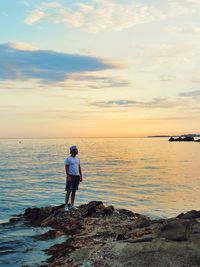 Man standing on rock by sea against sky during sunset