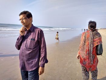 Friends standing on beach against sky