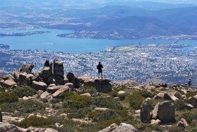 Rear view of hiker standing on rocks against cityscape
