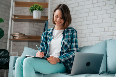 Young woman using phone while sitting on laptop