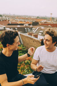 Man showing mobile phone to friend having drink at terrace during party