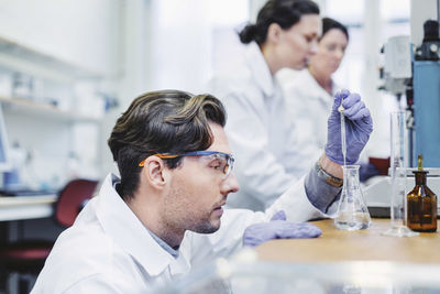 Male scientist examining sample at laboratory with female colleagues in background