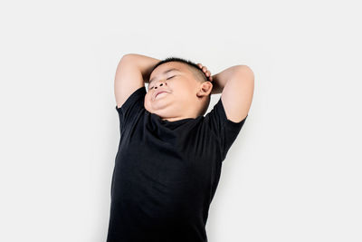 Boy with hands behind head standing against gray background