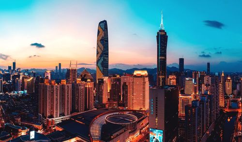 Illuminated modern buildings in city against sky during sunset