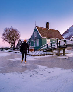 Rear view of man walking on snow covered building against sky