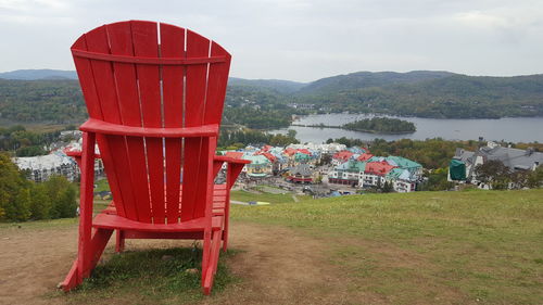 Red chairs on land by lake against sky