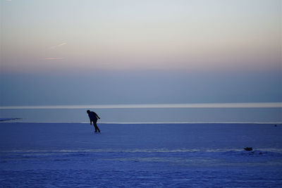 Man ice-skating by sea on snow during sunset