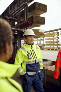 Female engineer with hands in pockets standing at lumber industry
