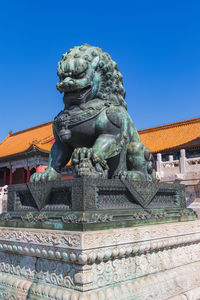 Low angle view of statue against building against clear blue sky