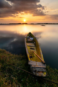 Abandoned boat moored on shore against sky during sunset