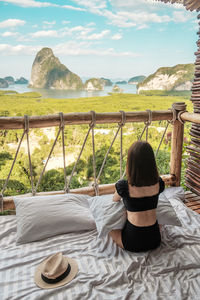 Rear view of woman sitting on railing against sky