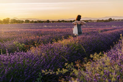 Woman standing on field against sky during sunset