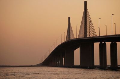 Low angle view of bridge over sea against orange sky