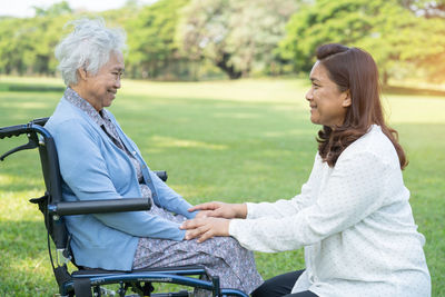 Caregiver help and care asian senior woman patient sitting and happy on wheelchair in park