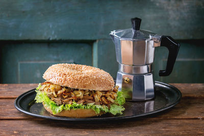 Close-up of burger and coffee maker in tray on wooden table