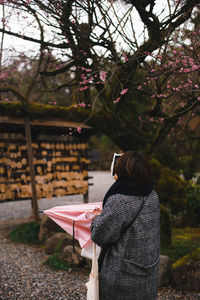 Rear view of woman standing by book against trees