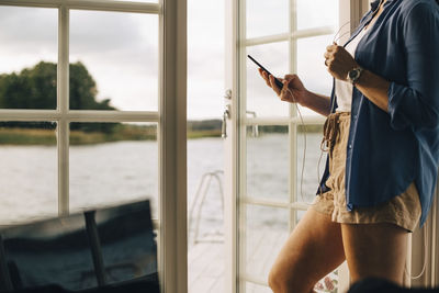 Midsection of mature woman listening music through headphones on smart phone at holiday villa