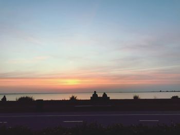 Silhouette people by sea against sky during sunset