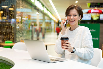 Happy woman with disposable cup talking on smart phone