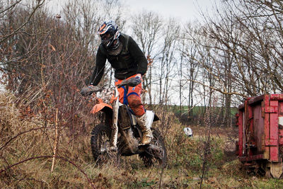 Person riding motocross on field against bare trees
