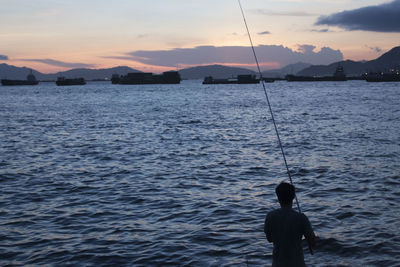 Silhouette man fishing in sea against sky
