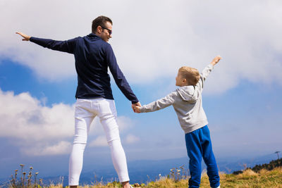 Rear view of son with father against sky