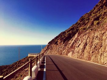 Road by sea against clear blue sky