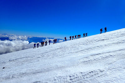 Row of hikers walking on snowcapped mountain against blue sky