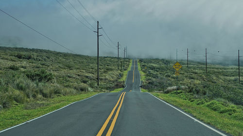 Road amidst electricity pylon against sky