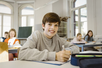 Portrait of happy schoolboy sitting at desk in classroom