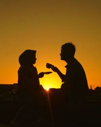 Silhouette man sitting against orange sky during sunset