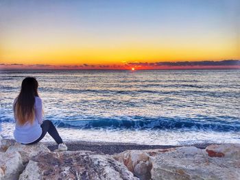 Woman sitting on beach against clear sky during sunset