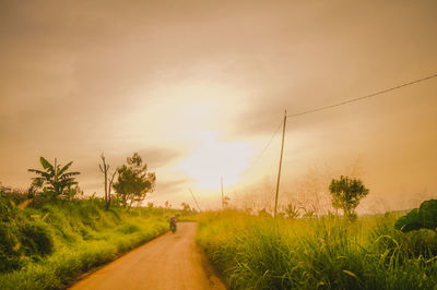 Road amidst field against sky during sunset