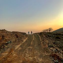 Rear view of people walking on landscape against sky during sunset
