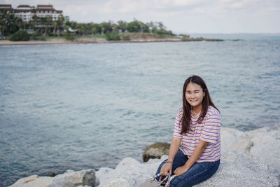 Portrait of young woman sitting on rock by sea