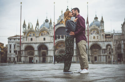 Young couple kissing while standing on town square in city