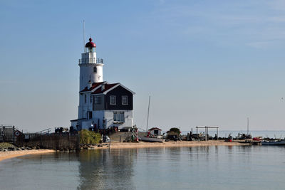 Lighthouse amidst buildings by sea against sky
